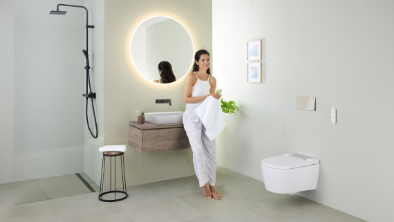 Woman leaning on a washbasin in a bathroom with Geberit AquaClean Sela shower toilet. Woman leaning on a washbasin in a bathroom with Geberit AquaClean Sela shower toilet.